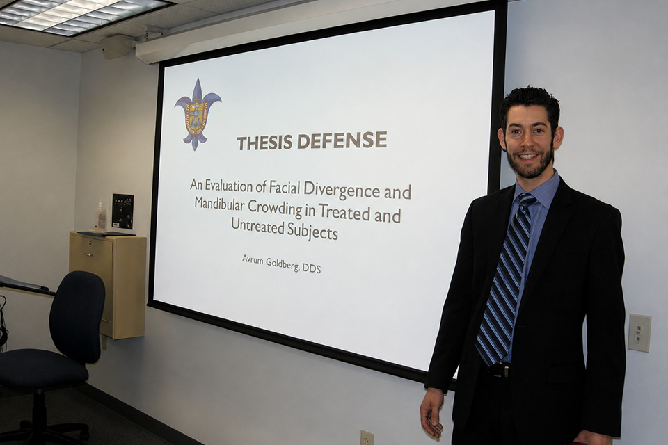 Avi Goldberg A man wearing a suit stands in front of a classroom and projector screen.