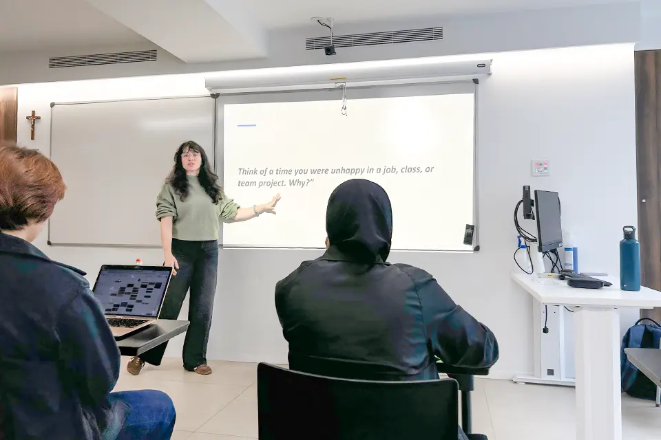 SLU-Madrid Alumna and Psychology Professor Valeriya Sidelkivska, Ph.D., Joins Faculty Full-Time Professor stands at the front of a classroom speaking with students seated at desks. A projector screen displays "Think of a time you were unhappy in a job, class or team project. Why?