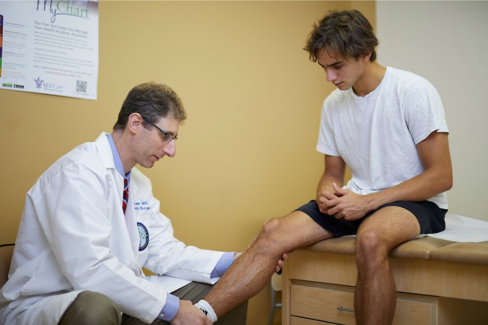 A sports medicine physician examines an athlete's leg in an office.