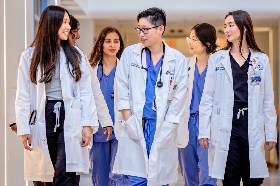 A group of internal medicine residents talk with one another while walking down a hospital hallway.