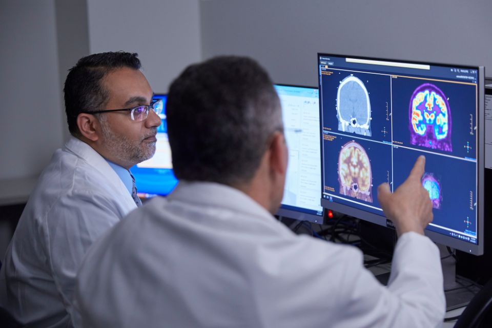 Two doctors examine a patient's nuclear medicine imaging results on a computer screen.