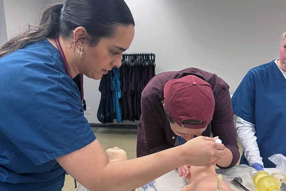 a woman in blue scrubs using a needle to insert a needle into a dummy