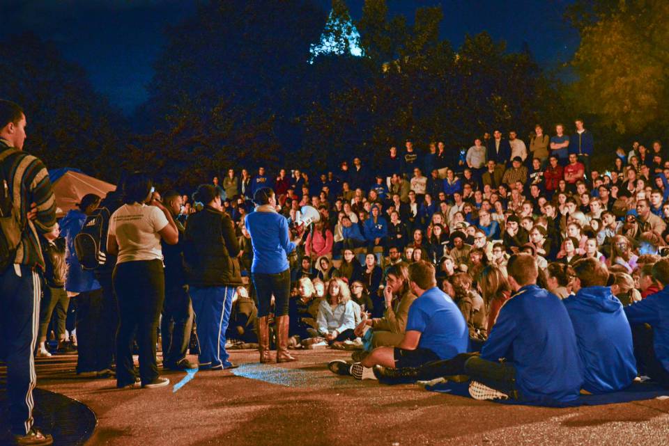 Students crowd around the clock tower plaza while listening to a speaker on a microphone